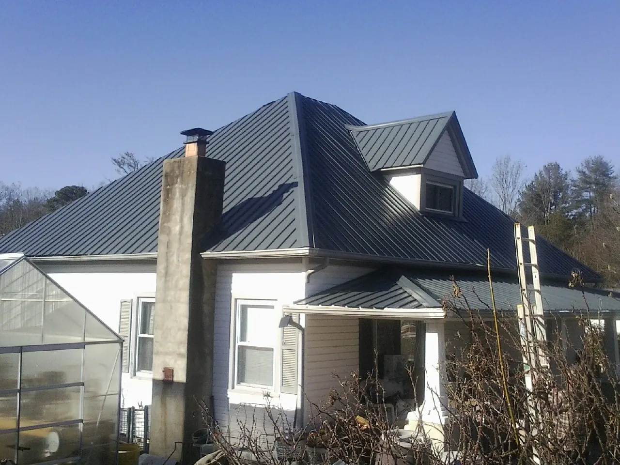 Dark blue standing seam metal roof on a white farmhouse with dormer — Slate & Tile Roof Repair by Roofing Brothers in Demarest