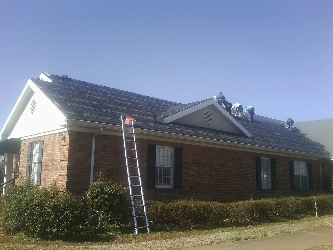 Crew tearing shingles off a brick ranch roof with a ladder set — Metal Roof Repair work by our crew in Demarest