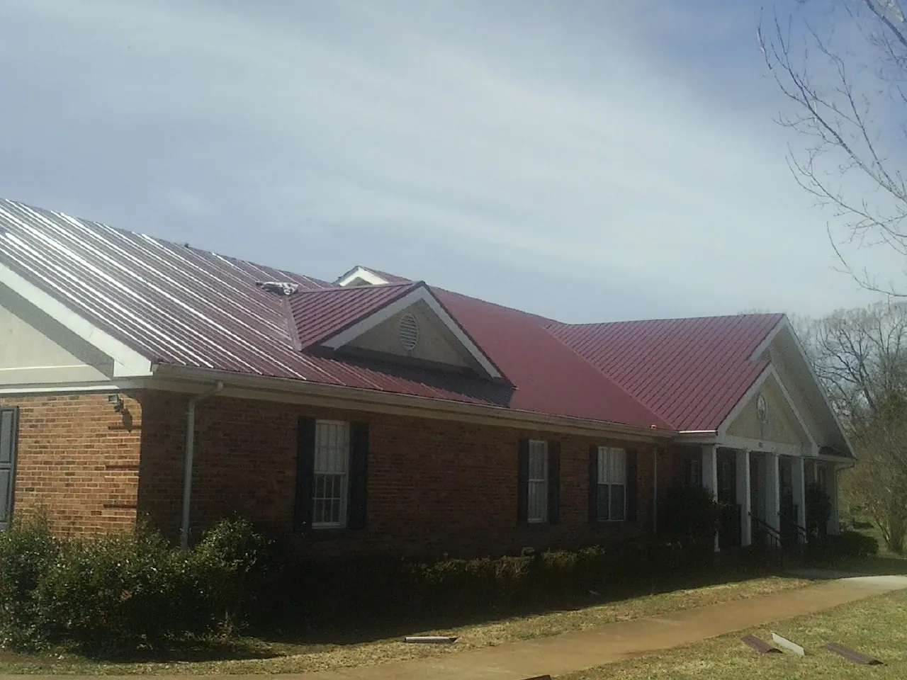 Red metal roof with gabled entries on a long brick building, from a Hail Damage Roof Repair job in Demarest