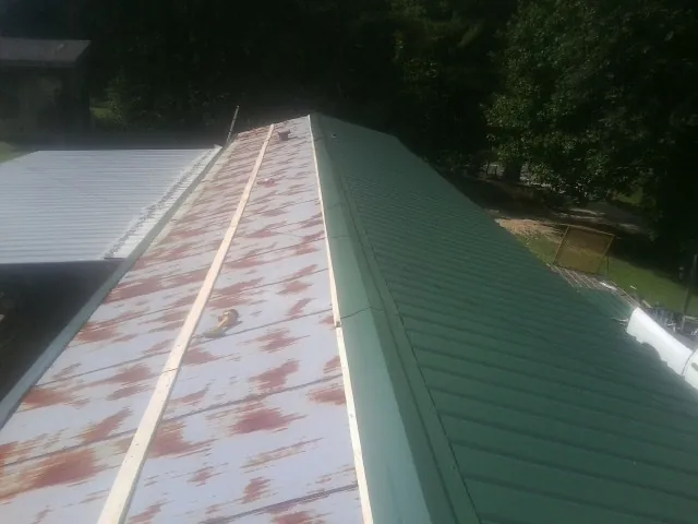 Old rusted panels beside newly installed green metal roofing — Wind Damage Roof Repair by Roofing Brothers in Demarest