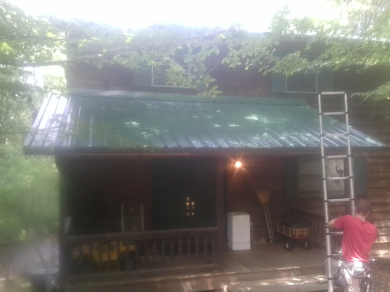 Worker on a ladder at the green porch roof of a wooded cabin in Demarest