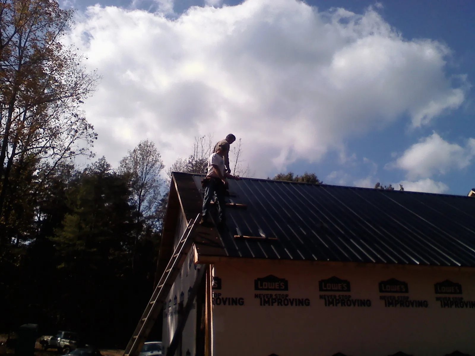 Roofer fastening dark metal panels high against a cloudy sky, from a Roof Inspection job in Demarest